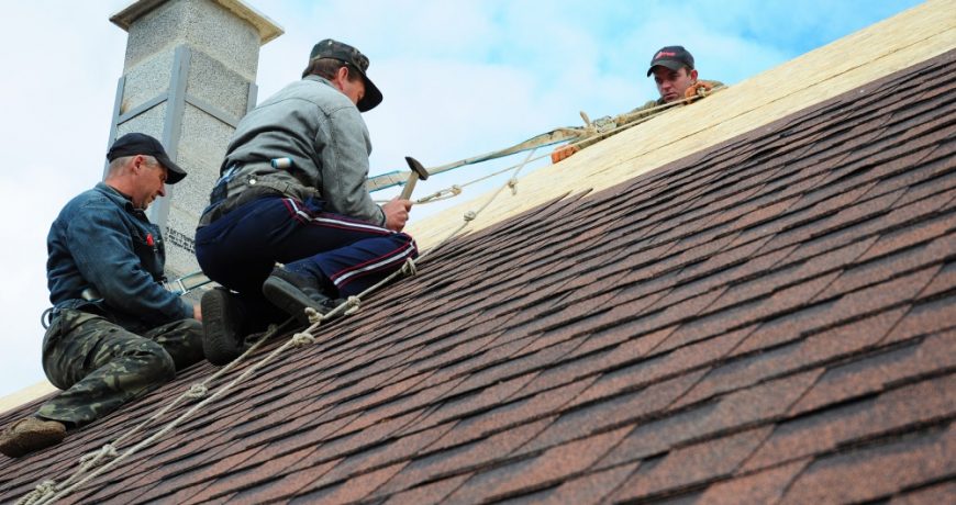 KIEV - UKRAINE MAY - 8  2017: Roofing Construction. Roofing Contractors Install New House Roofing with Asphalt Shingles Roofing Construction. Roofers with safety rope. Roofing Contractor.